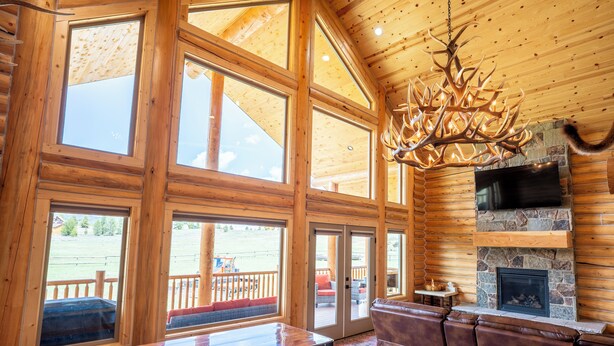 A spacious lodge with large windows, a stone fireplace, and a wooden ceiling. - 35 Minutes from Yellowstone Lux Log Home with Hot Tub, Pool Table, and Firepit.  (Island Park)