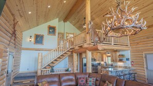 A log cabin interior with a wooden staircase, a leather sofa, and a chandelier made of antlers. - 35 Minutes from Yellowstone Lux Log Home with Hot Tub, Pool Table, and Firepit.  (Island Park)