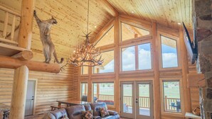 A log cabin interior with a leather sofa, a chandelier, and a mounted animal head. - 35 Minutes from Yellowstone Lux Log Home with Hot Tub, Pool Table, and Firepit.  (Island Park)