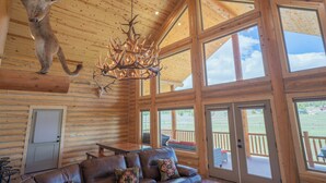 A log cabin interior with a leather sofa, a chandelier, and a mounted animal head. - 35 Minutes from Yellowstone Lux Log Home with Hot Tub, Pool Table, and Firepit.  (Island Park)