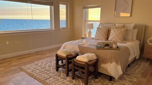 A bedroom with a large bed, two chairs, a nightstand, and a view of the ocean. - Private Waterfront Beach House with Fire-pit (Ocean Springs)