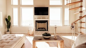 A living room with a fireplace, a sofa, a coffee table, and a TV. - Private Waterfront Beach House with Fire-pit (Ocean Springs)