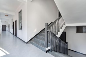 Un interior moderno con una escalera recta, un largo pasillo y una puerta al final.