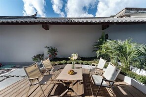 An outdoor dining area with a wooden table and chairs, surrounded by potted plants and a tiled roof. - YUNZHINAN HOTEL (Lijiang)