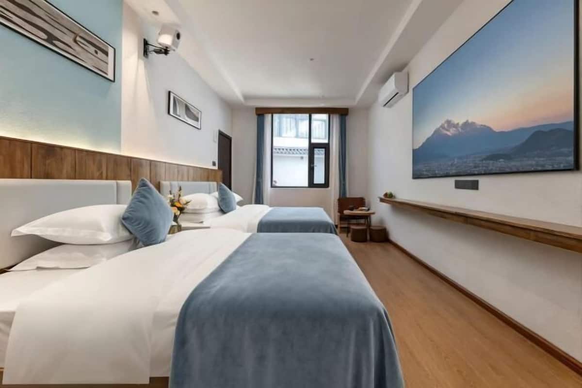 A hotel room with two beds, a large window, a painting, and a small table.