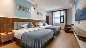Quarto de hotel com duas camas, cabeceira de madeira, uma mesinha com uma cadeira e uma janela grande.