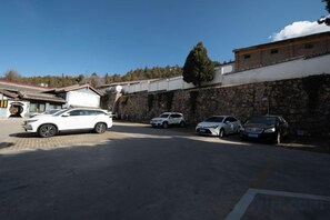 A parking area with several cars, a building with a tiled roof, and a stone wall. - YUNZHINAN HOTEL (Lijiang)