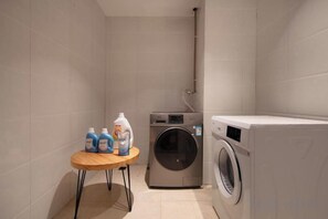 A compact laundry room with a washing machine, a dryer, and a small table with cleaning supplies. - YUNZHINAN HOTEL (Lijiang)