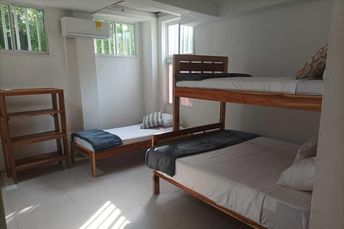 A dormitory room with bunk beds, a wooden shelf, a window, and an air conditioning unit.