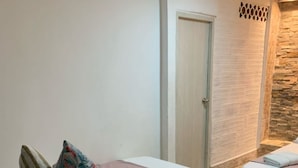 A hotel room with a bed, pillows, a bedside table, a door, and a stone wall. - Hostal Catalleya (Cartagena)