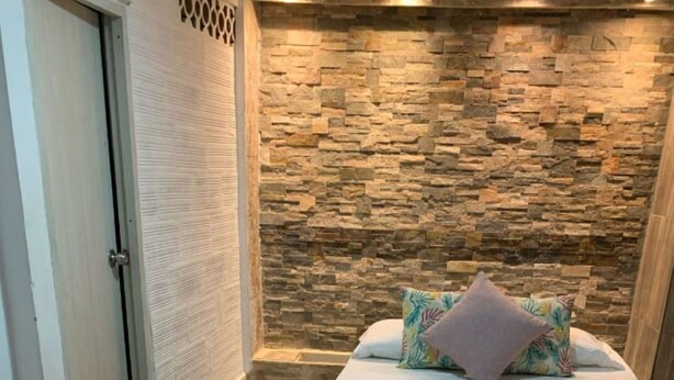 A hotel room with a stone wall, a bed with pillows, and a towel on the bed. - Hostal Catalleya (Cartagena)