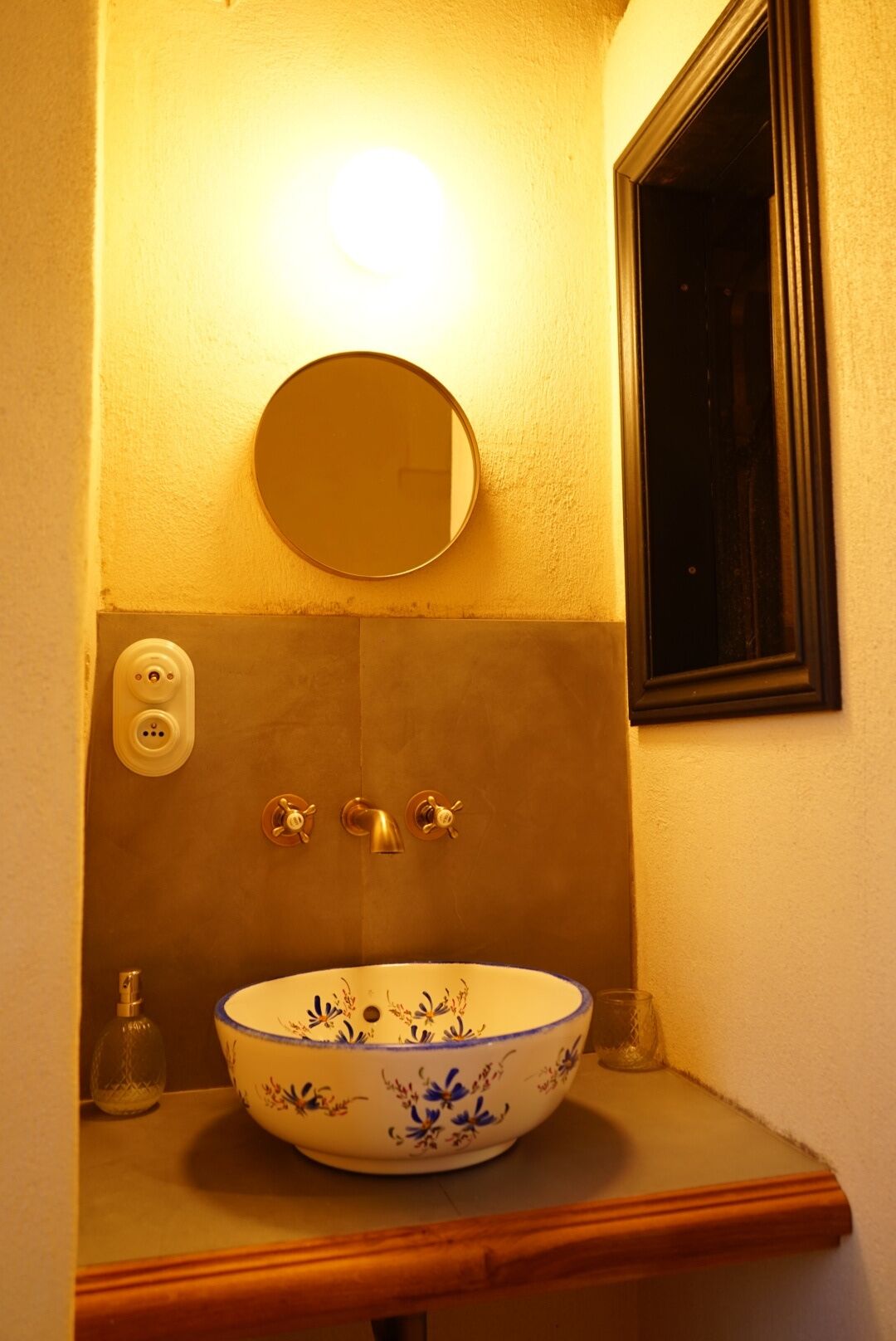 Un baño con un espejo redondo, un lavabo blanco con motivos florales azules y una encimera de madera.