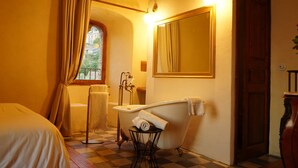 Une salle de bain avec une baignoire, un lavabo et un miroir. Il y a une fenêtre avec des rideaux, une porte et un sol à carreaux.