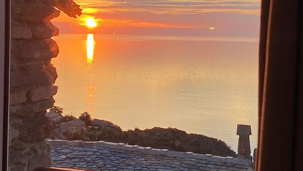 Une vue sur le coucher de soleil depuis un balcon aux murs de pierre et au toit recouvert de tuiles.