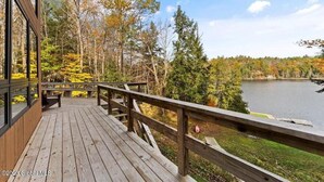 A wooden deck with a railing overlooking a lake surrounded by trees. - Beautiful lakefront house on Paradox lake with tremendous views and privacy. (Paradox)
