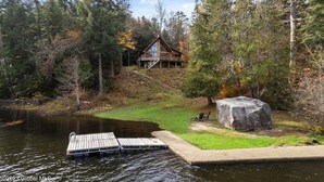 A cabin with a dock extending into a lake, surrounded by trees and a large rock. - Beautiful lakefront house on Paradox lake with tremendous views and privacy. (Paradox)