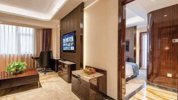A hotel room with a large bed, a desk with a computer, a TV mounted on the wall, and a small table with fruit. - Ying Rong Hotel (Chuxiong City)