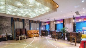 A modern hotel lobby with a marble floor, a central seating area with a sofa and chairs, a reception desk, and a colorful mural on the wall. - Ying Rong Hotel (Chuxiong City)