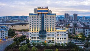 A multi-story hotel with a central atrium, surrounded by a landscaped area with trees. - Ying Rong Hotel (Chuxiong City)
