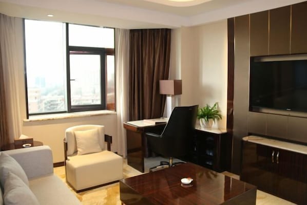 A modern hotel room with a large window, a sofa, a desk, a chair, a coffee table, and a TV.