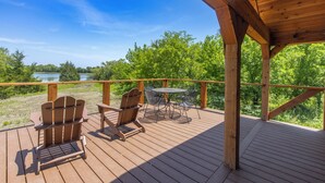 Une terrasse en bois avec des fauteuils Adirondack et une table, offrant une vue sur un lac et une forêt.