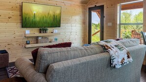 Un salon chaleureux avec un grand téléviseur à écran plat fixé à un mur en bois, un canapé avec une couverture et une petite plante posée sur une étagère.