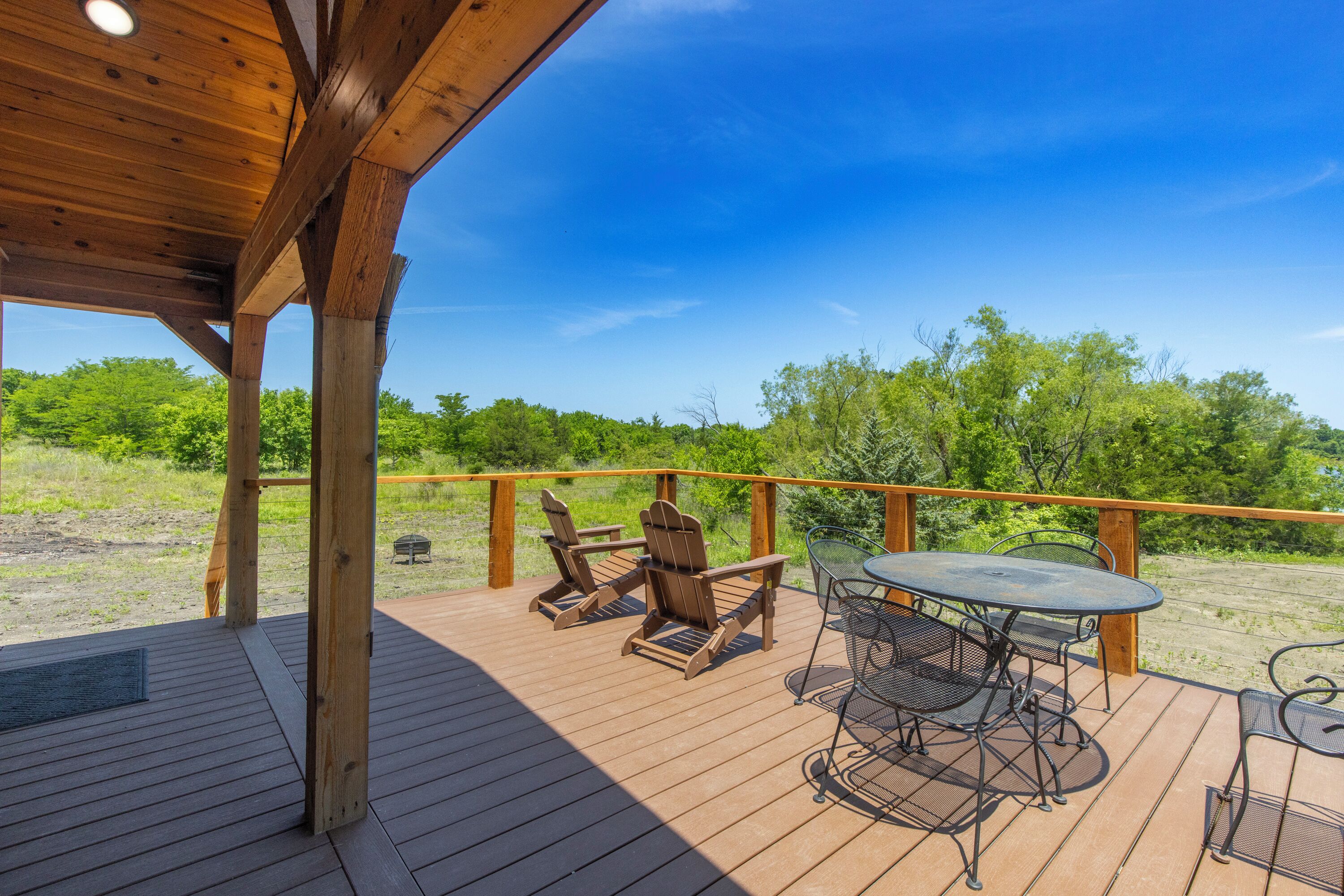 A wooden deck with outdoor seating, including chairs and a table, overlooking a grassy area with trees.