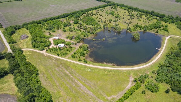 Luchtbeeld van een landelijk gelegen bezit met een groot meer, omgeven door weelderige begroeiing en enkele gebouwen.