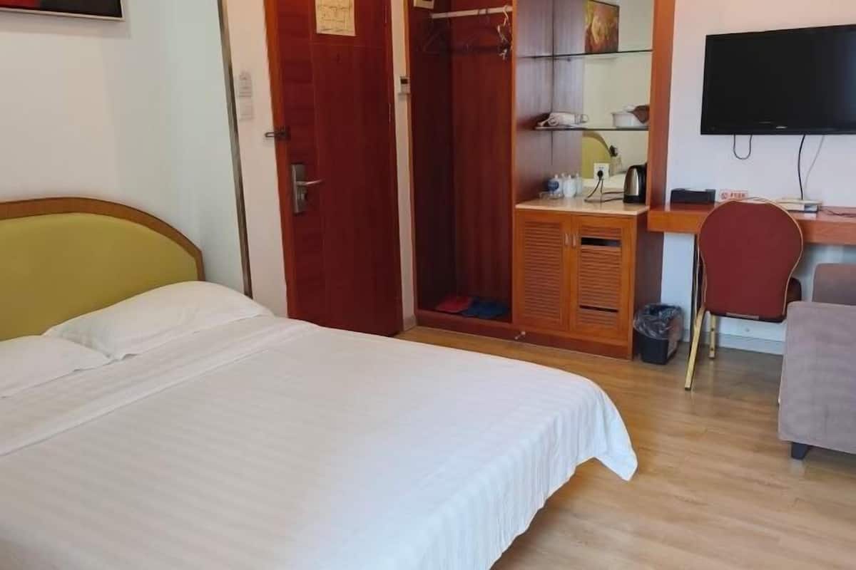 A hotel room with a bed, a wooden desk, a television, and a wardrobe.