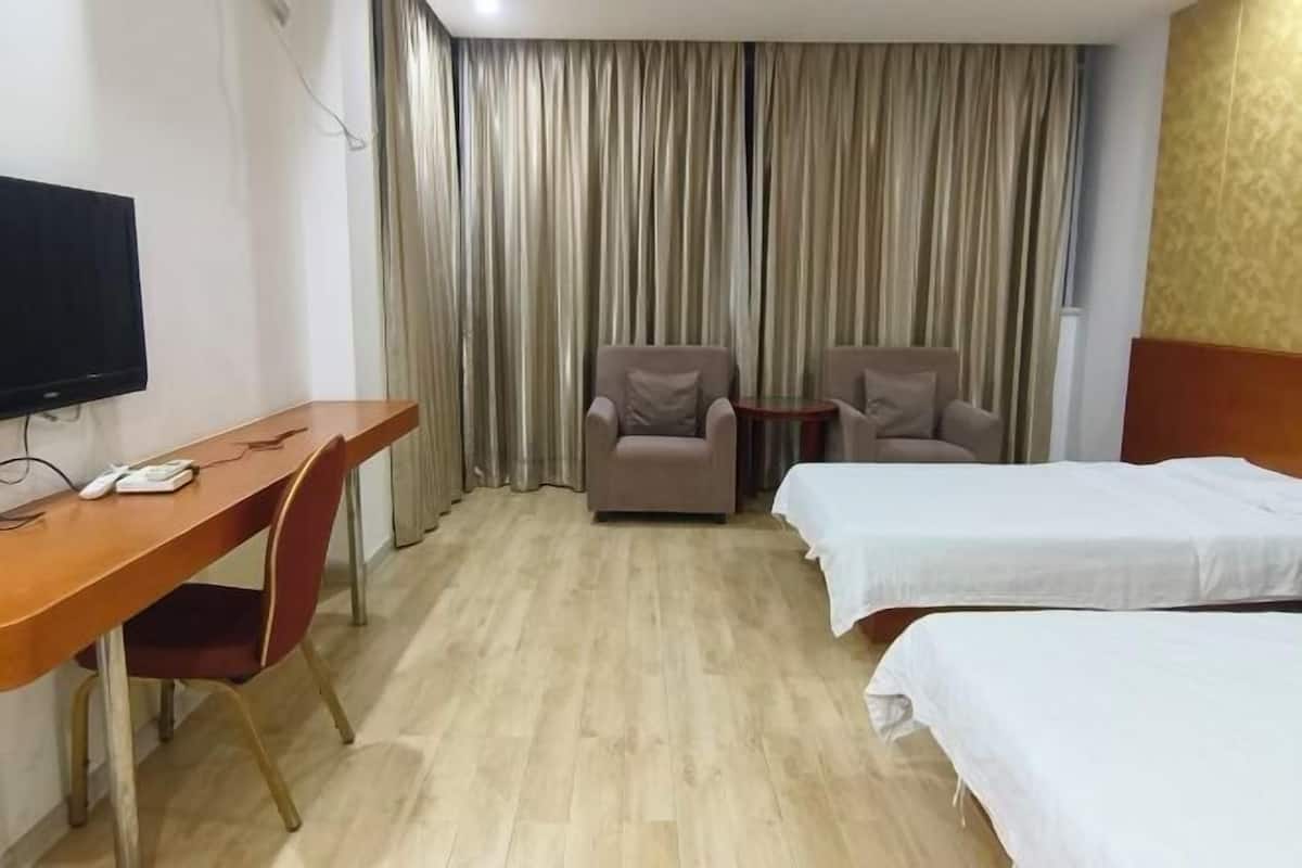 A hotel room with a wooden desk, two armchairs, a TV, and two beds.