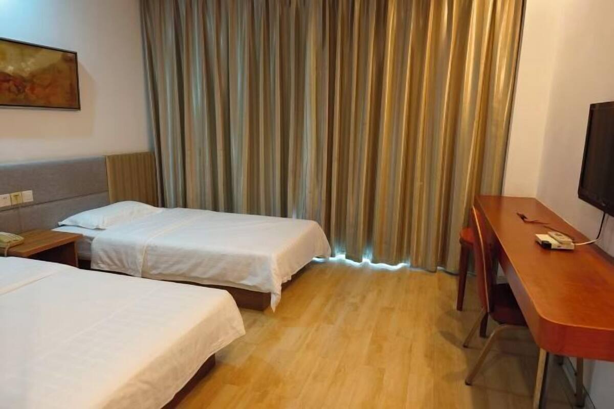 A hotel room with two single beds, a wooden desk, a television, and a curtain.