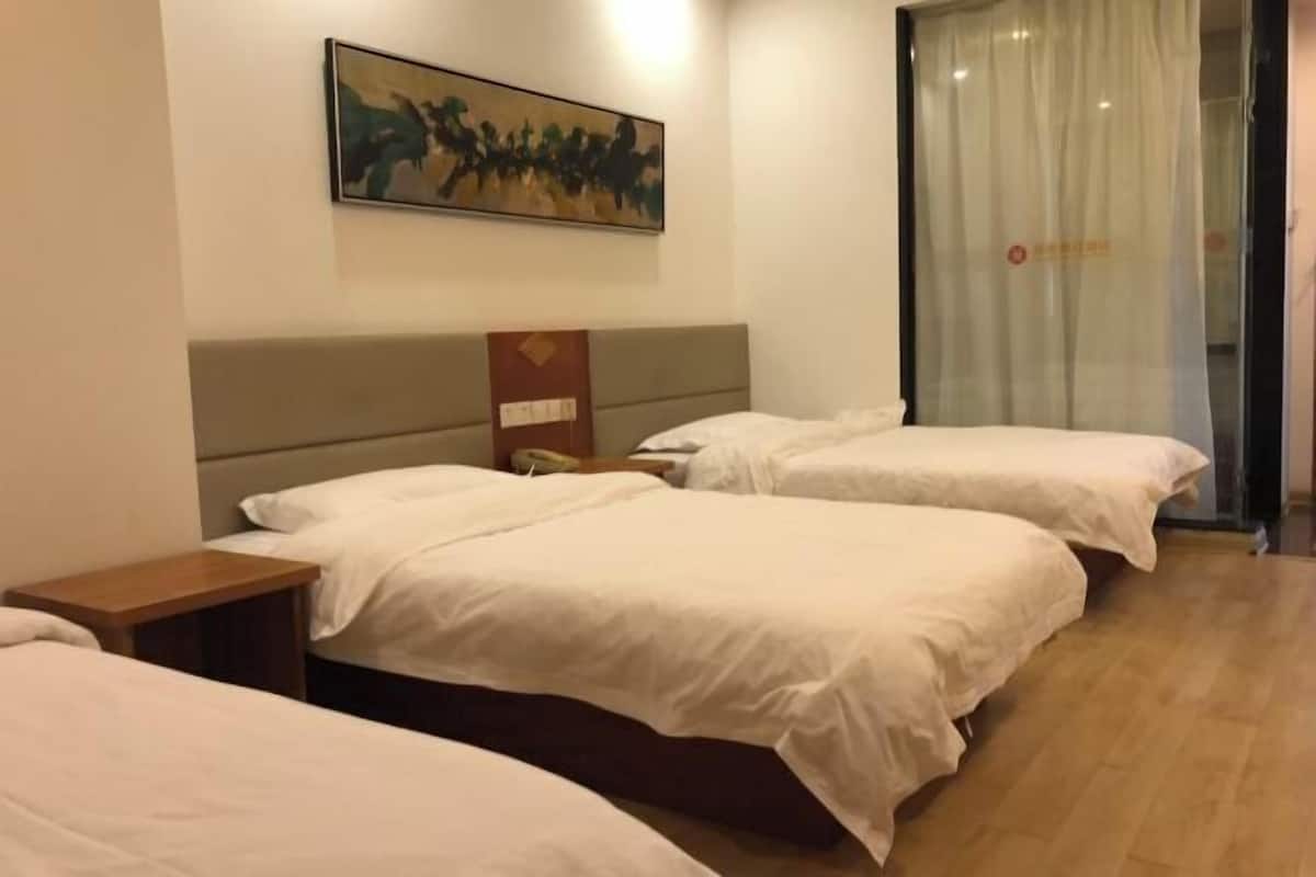 A hotel room with two beds, a painting on the wall, a nightstand, and a glass door with curtains.