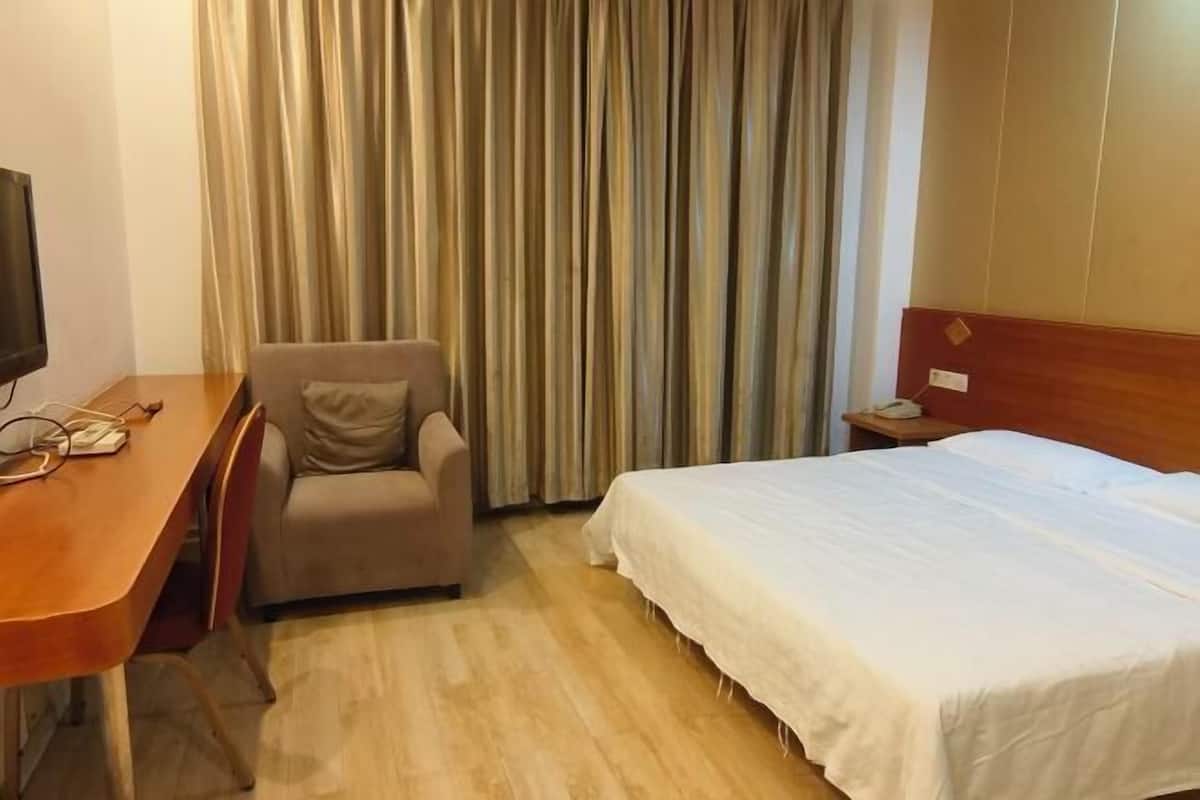 A hotel room with a wooden desk, a chair, a bed, and a curtain.