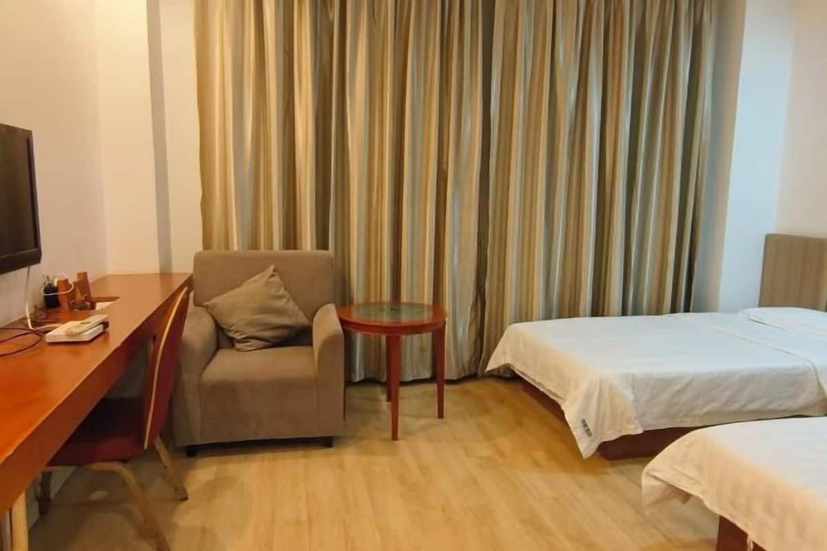 A hotel room with a wooden desk, a chair, a small round table, and two beds with white bedding.