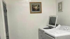 Un lavadero con lavadora y secadora, una puerta y un cuadro en la pared.