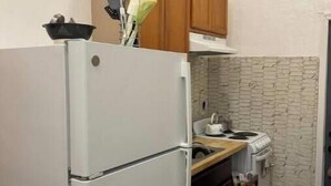 Una cocina compacta con un refrigerador blanco, armarios de madera, protector contra salpicaduras de piedra y una estufa pequeña.