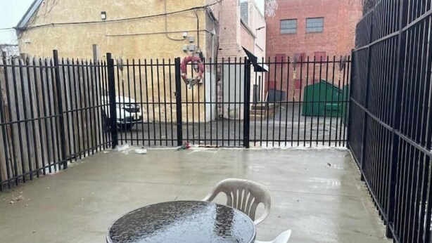 Un patio con una mesa redonda y sillas, rodeado por una valla de metal negro.