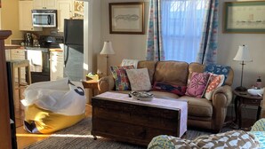 A living room with a sofa, a patterned armchair, a coffee table, and a kitchen in the background. - Whale Ledge Cottage - In the heart of Lubec with AMAZING Waterviews!  (Lubec)