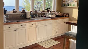 A kitchen with a large window, wooden cabinets, a sink, and a bar stool. - Whale Ledge Cottage - In the heart of Lubec with AMAZING Waterviews!  (Lubec)