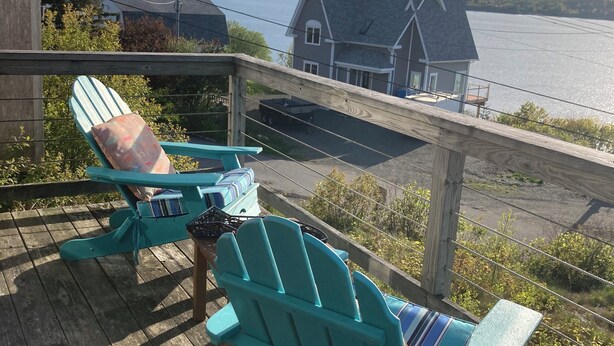A wooden deck with turquoise Adirondack chairs and a table, overlooking a lake and a house. - Whale Ledge Cottage - In the heart of Lubec with AMAZING Waterviews!  (Lubec)