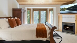 Une chambre avec un grand lit, un plafond en bois, une cheminée et un téléviseur.