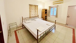 Habitación con una cama individual, estructura de metal, ventilador de techo, ventana con cortinas, armario de madera y una puerta.