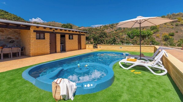 Una piscina con hidromasaje, rodeada de césped y un edificio de ladrillo.