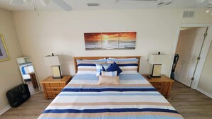 Un dormitorio con una cama grande, dos mesitas de noche, una mesilla auxiliar, un cuadro colgado en la pared y una puerta.