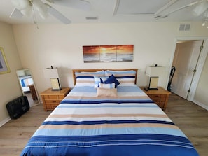 A bedroom with a large bed, two bedside tables, a nightstand, a wall-mounted painting, and a door.