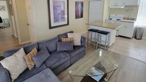 Una sala de estar moderna con un sofá seccional gris, una mesa de centro de vidrio y un ventilador de techo.