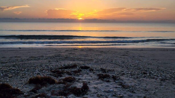 Una playa con un atardecer sobre el océano.