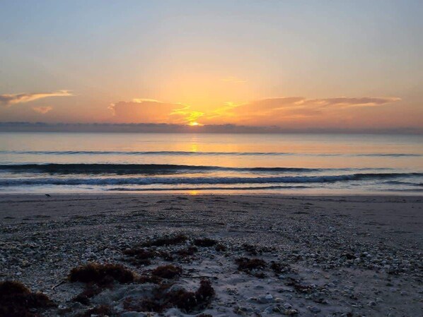 Una playa con un atardecer sobre el océano.