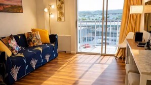 A modern living room with a sofa, a dining area, and a large sliding glass door leading to a balcony. - Newly Renovated Hilo Lagoon 2 BD Condo-A/C, Pool (Hilo)