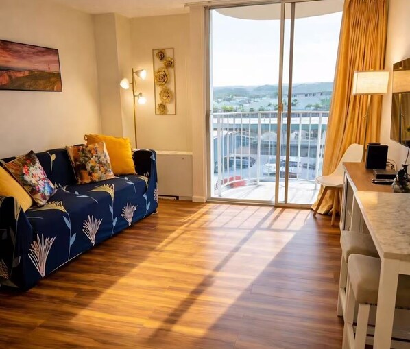 A modern living room with a sofa, a dining area, and a large sliding glass door leading to a balcony. - Newly Renovated Hilo Lagoon 2 BD Condo-A/C (Hilo)